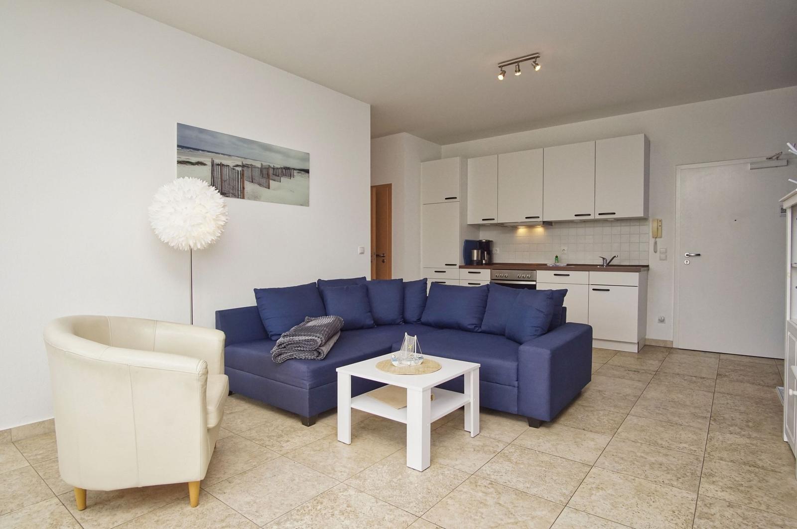 Wohnbereich mit blauem Sofa, weißem Tisch und Küchenzeile.