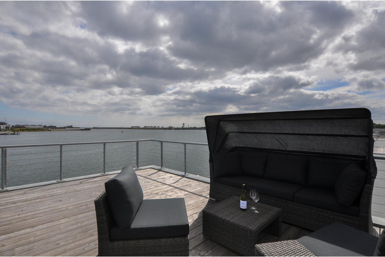 Terrasse mit Sitzgruppe und Blick auf Wasser und Himmel.