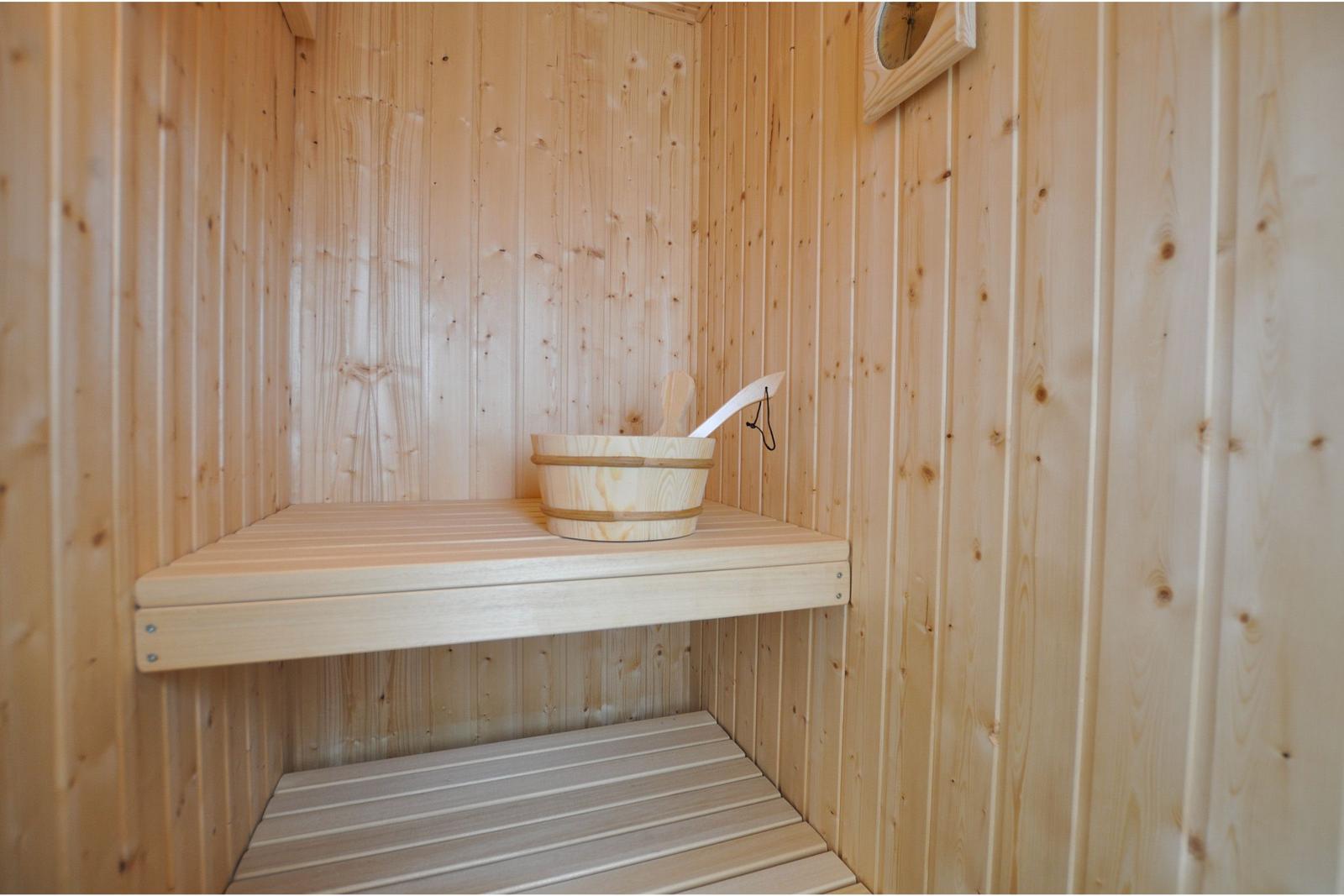 Sauna mit Holzbank und Eimer. Holzwand und Uhr sichtbar.