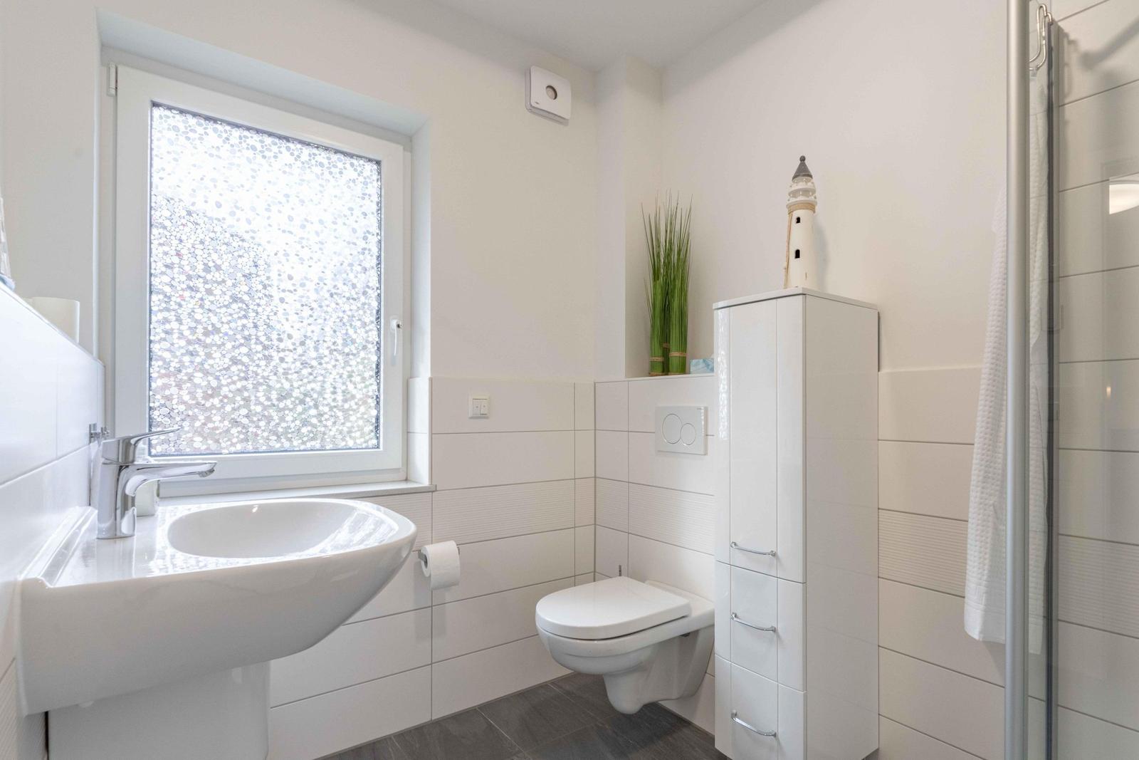 Badezimmer mit Waschbecken, Toilette und Dusche. Fenster mit Mosaikglas.