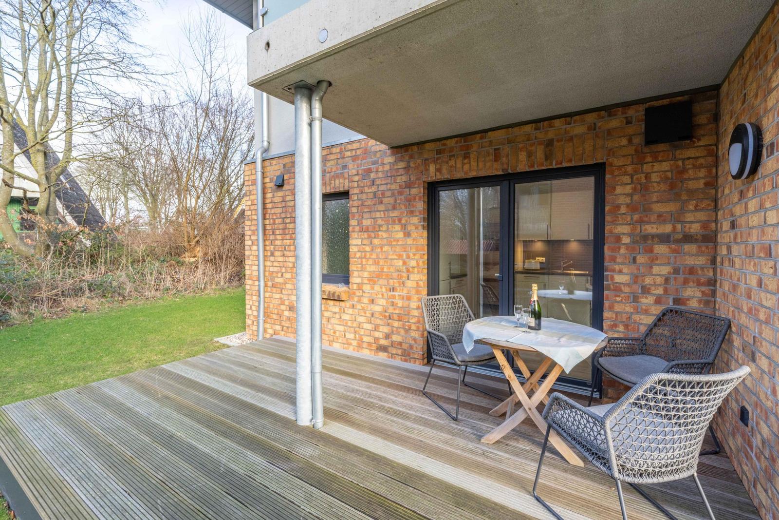 Terrasse mit Tisch und Stühlen, Blick in die Küche, Holzdecke und Backsteinwand.