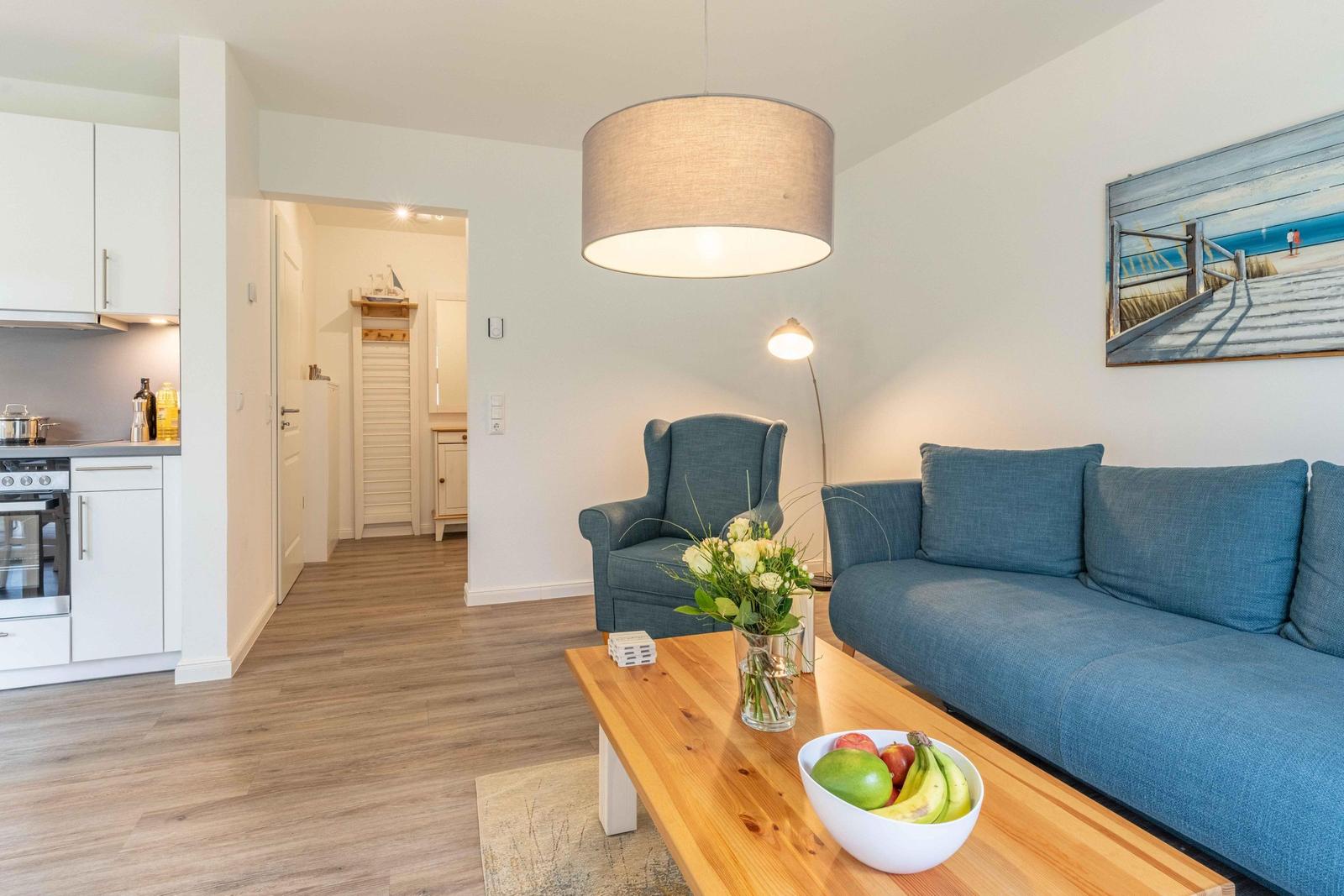 Wohnzimmer mit blauem Sofa, Holztisch und Küchenbereich im Hintergrund.