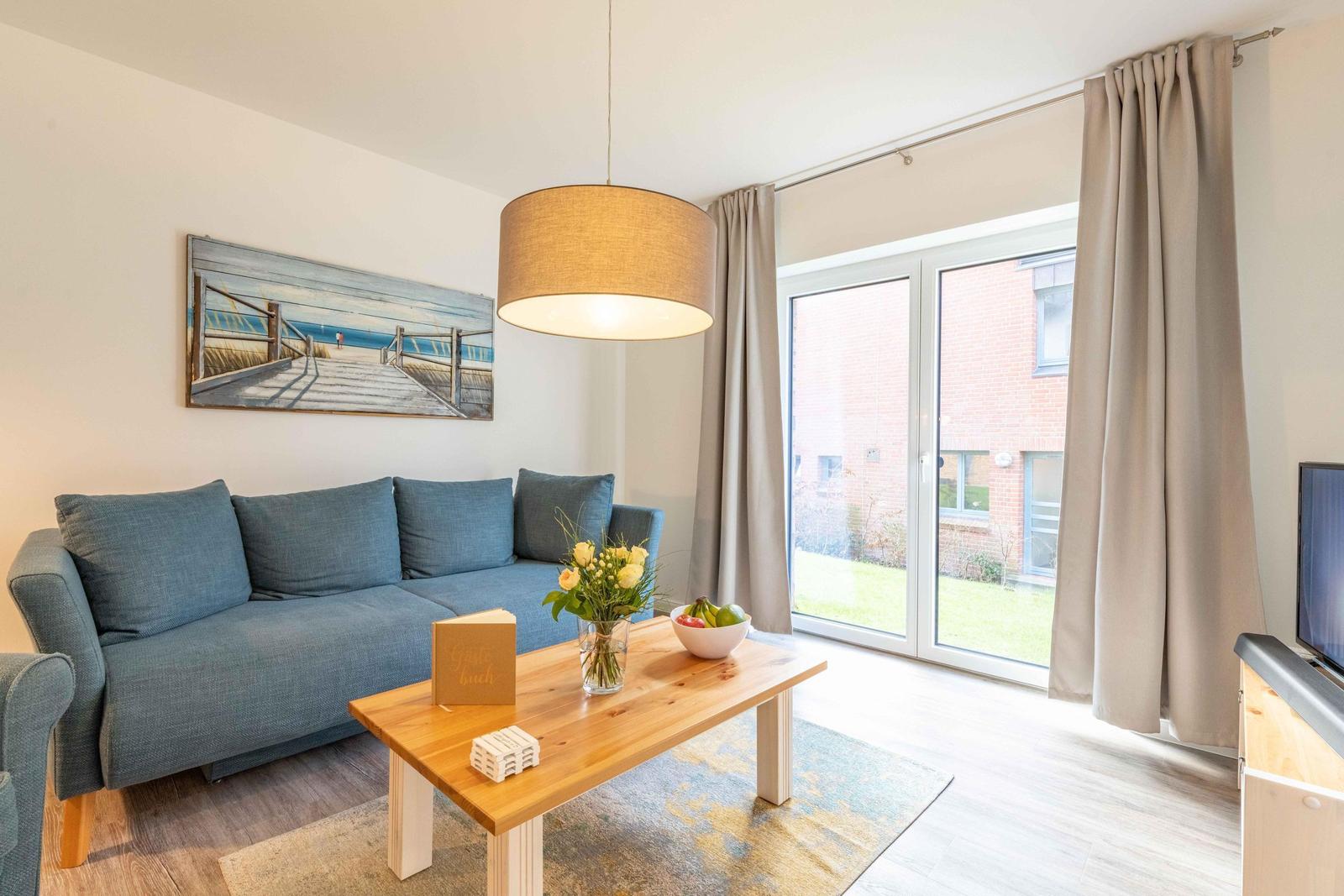 Wohnzimmer mit Sofa, Tisch und Fenster zur Terrasse.