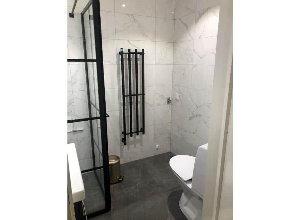 Bad mit Dusche, Toilette und Heizkörper an der Wand.