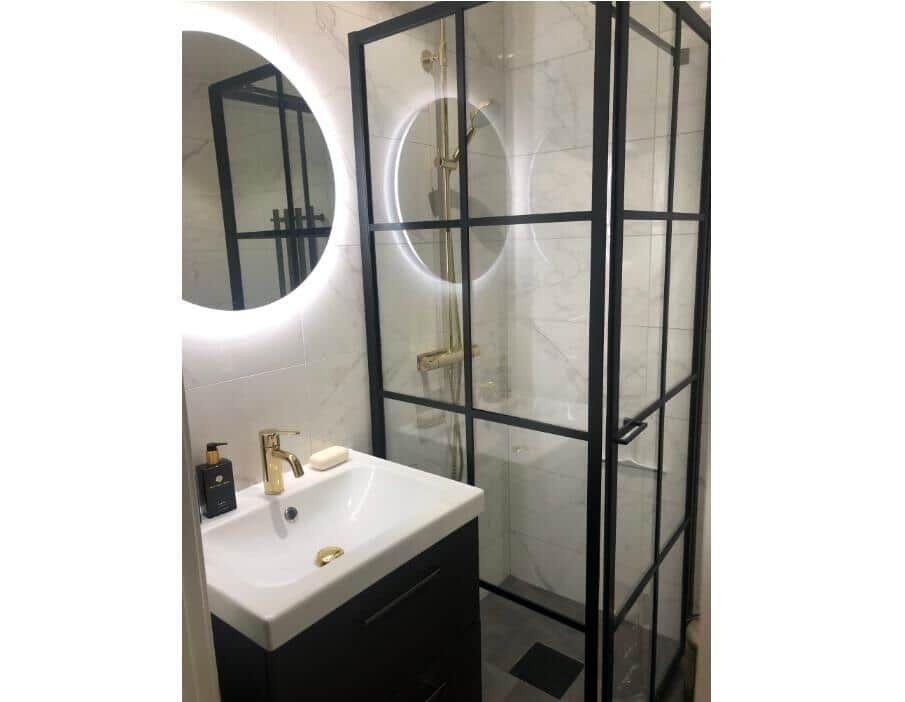 Badezimmer mit Duschkabine, Waschbecken und runden Spiegel mit Beleuchtung.