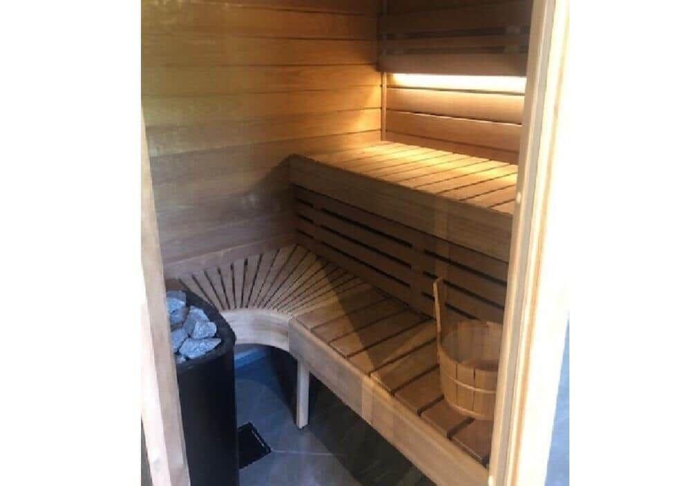 Sauna mit Holzbänken, Steinkachel und Eimer.