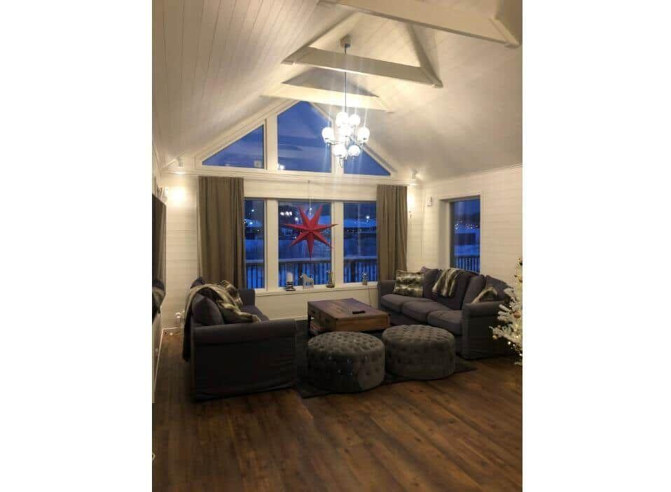 Wohnzimmer mit dunklen Sofas, Holzboden und hohem Dach. Fenster mit roter Sterndekoration.