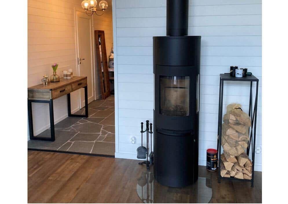 Schwarzer Kaminofen mit Holzstapel und Tisch im Eingangsbereich.