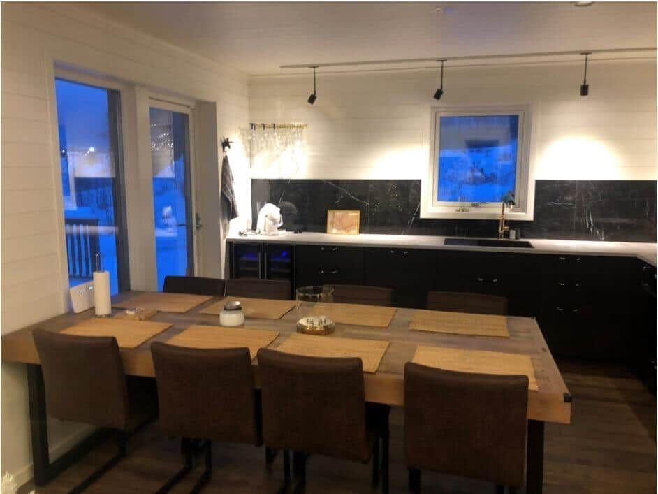 Essbereich mit Holztisch und Stühlen, Küchenzeile mit schwarzen Schränken und Fensterblick.