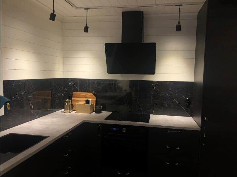 Küche mit schwarzen Schränken, Marmorwand und moderner Dunstabzugshaube.