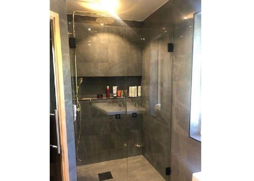 Duschkabine mit Glaswand und Duschkopf, dunkle Fliesen und integrierte Ablage