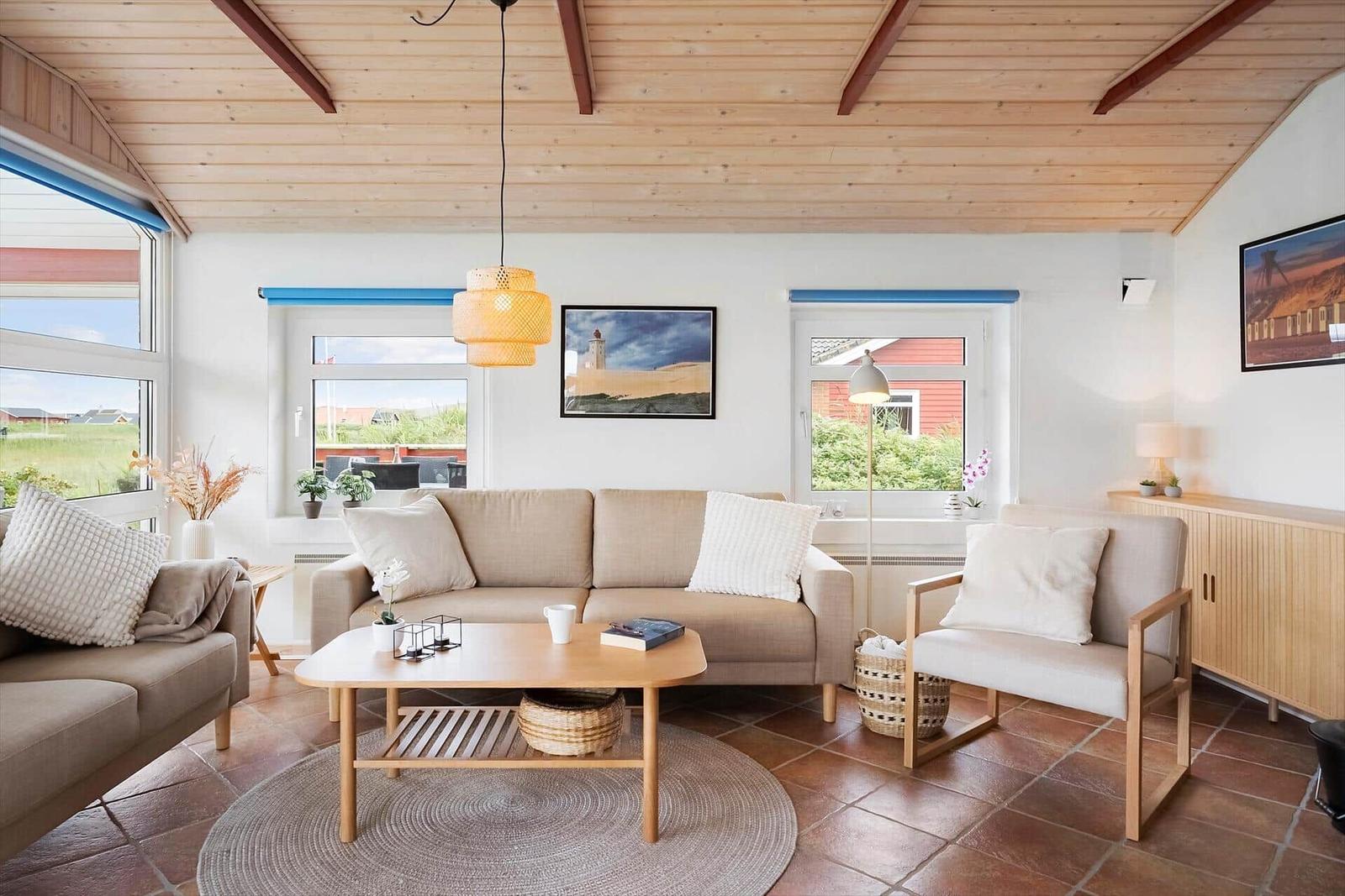 Wohnzimmer mit Sofa, Sessel und Tisch. Holzdecke und Fenster mit Blick.