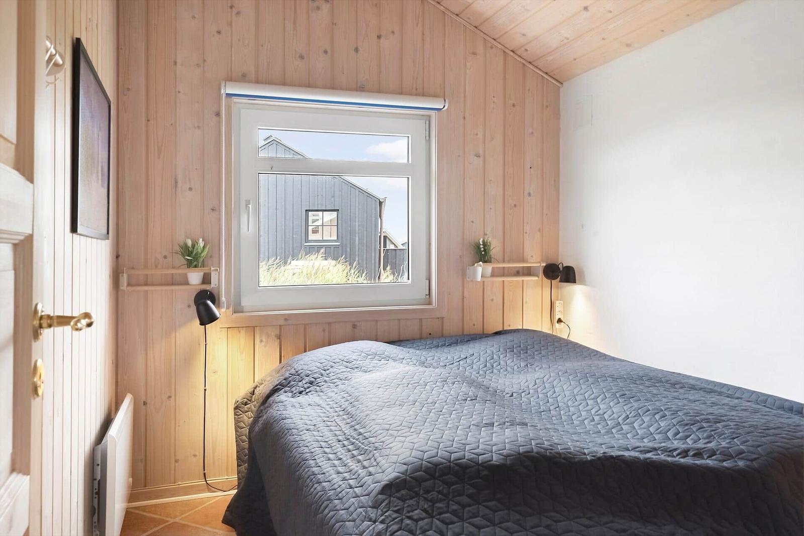 Schlafzimmer mit Holzwänden, Bett und Fensterblick auf Gebäude.