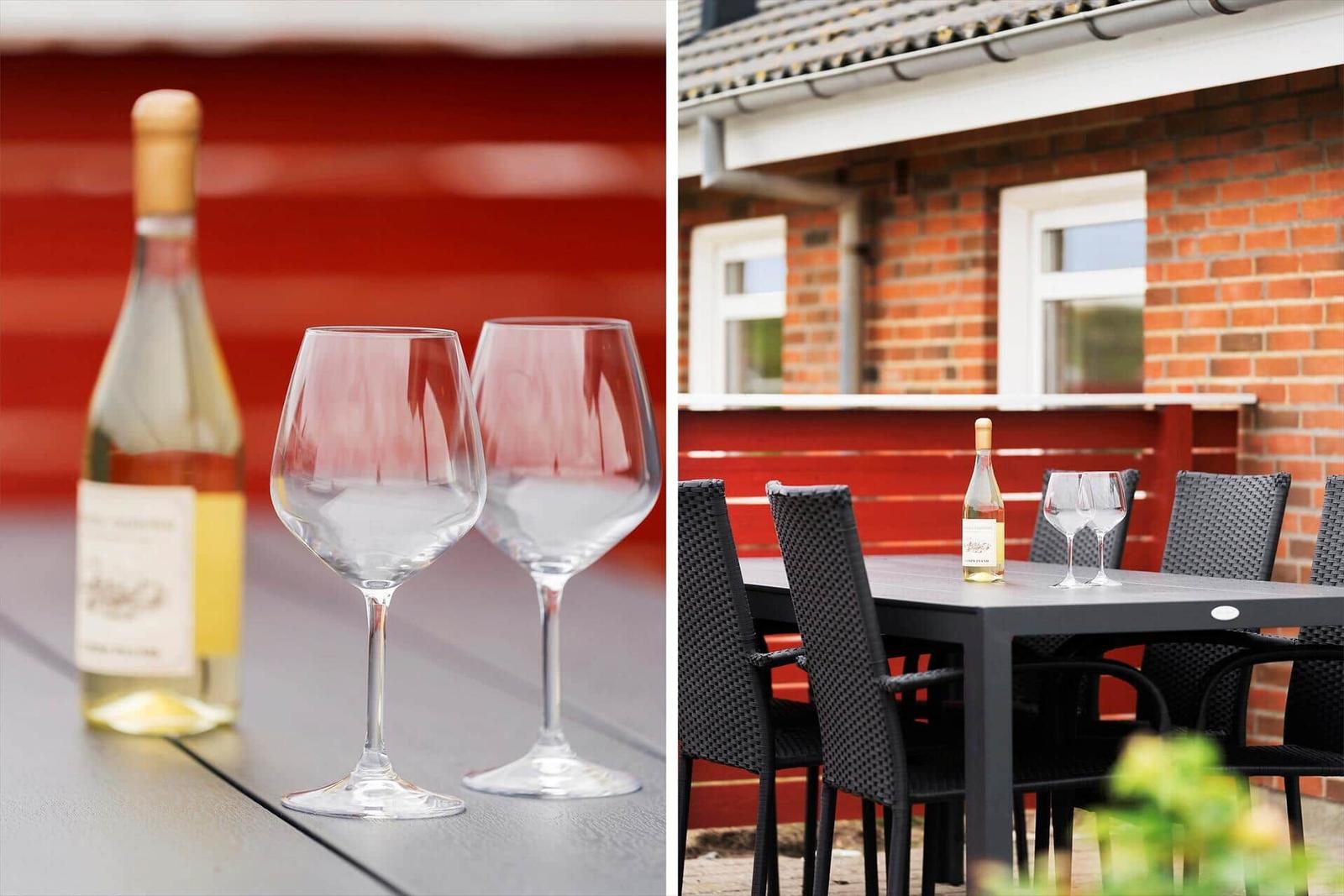 Außenbereich mit Tisch, Stühlen und Weinglas. Rot gestrichene Wand im Hintergrund.