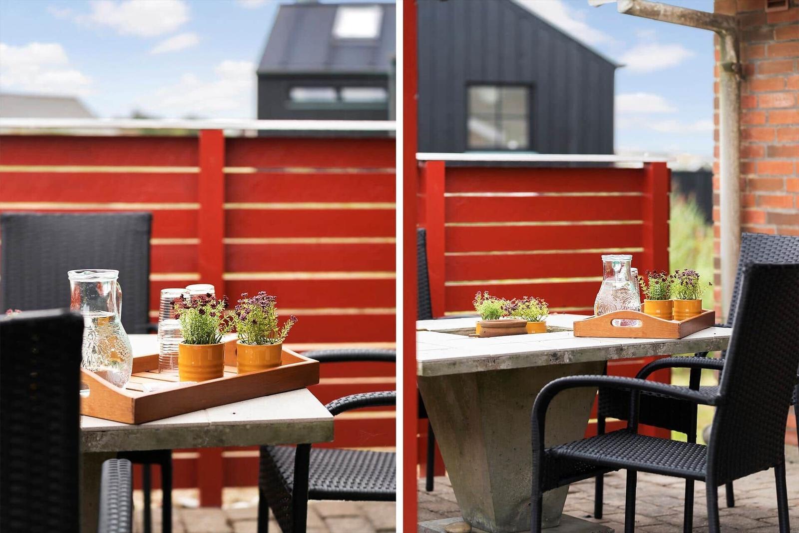 Terrasse mit Tisch, Stühlen und Pflanzen vor roter Holzabtrennung.