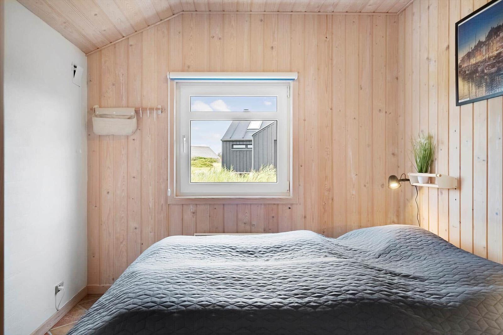Schlafzimmer mit Holzwand, Bett und Fensterblick auf Außenbereich.