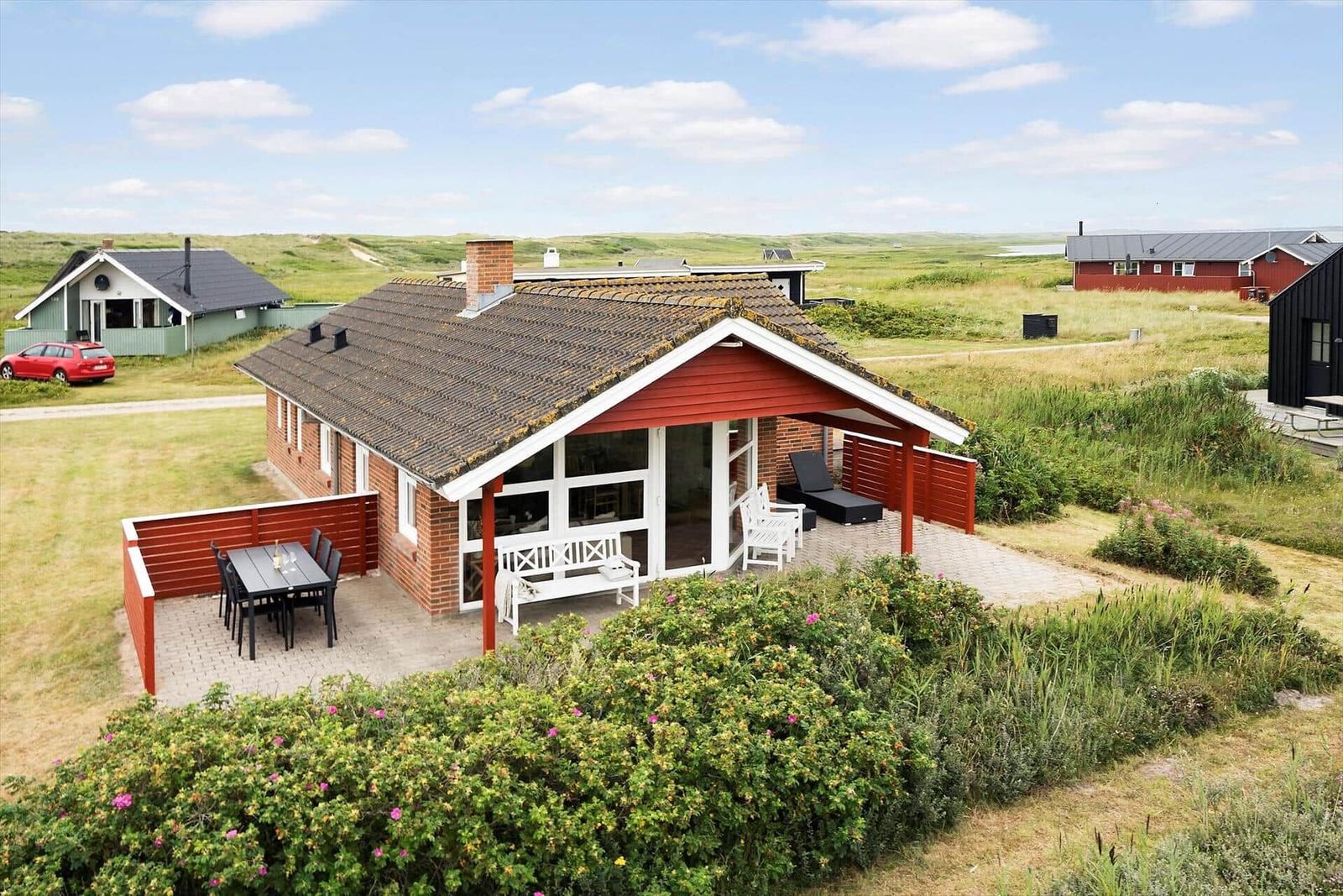 Rotes Ferienhaus mit Terrasse und Garten. Blick auf grüne Landschaft.