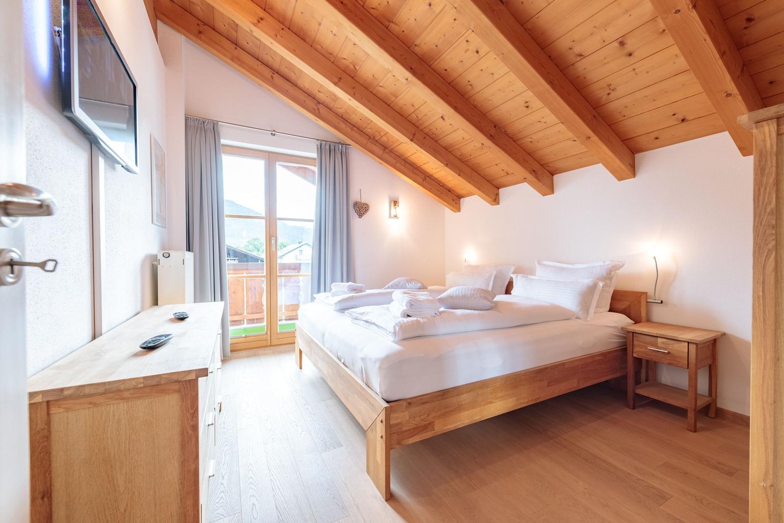 Schlafzimmer mit Holzboden, Dachschräge und Balkonzugang.