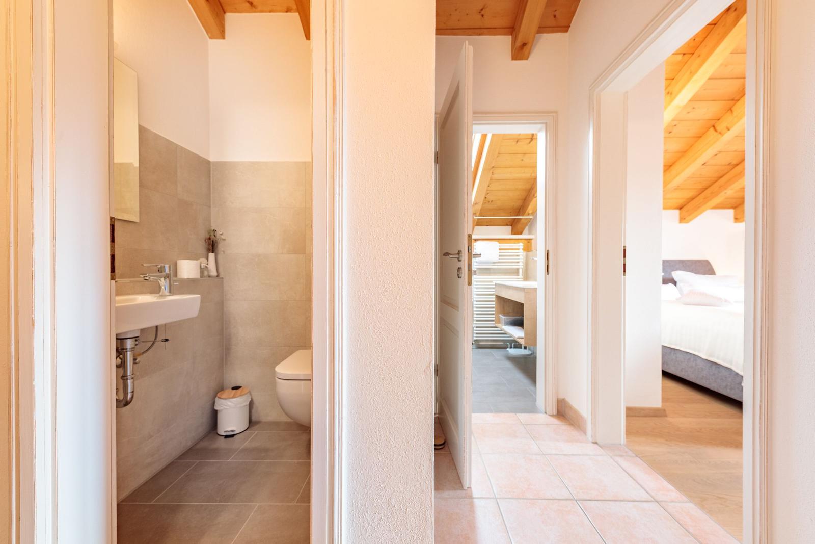 Badezimmer mit Toilette und Waschbecken. Durchgang zu Schlafzimmer und Dusche.