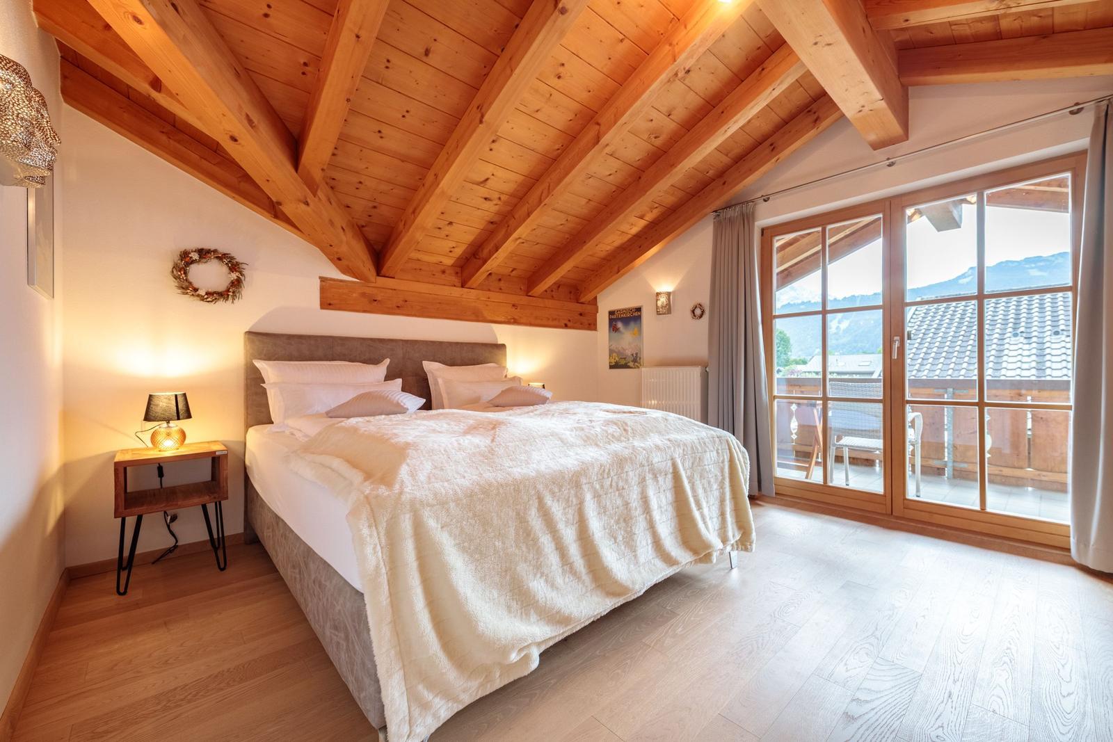 Schlafzimmer mit Holzboden, Balkon und Holzdecke mit Balken.