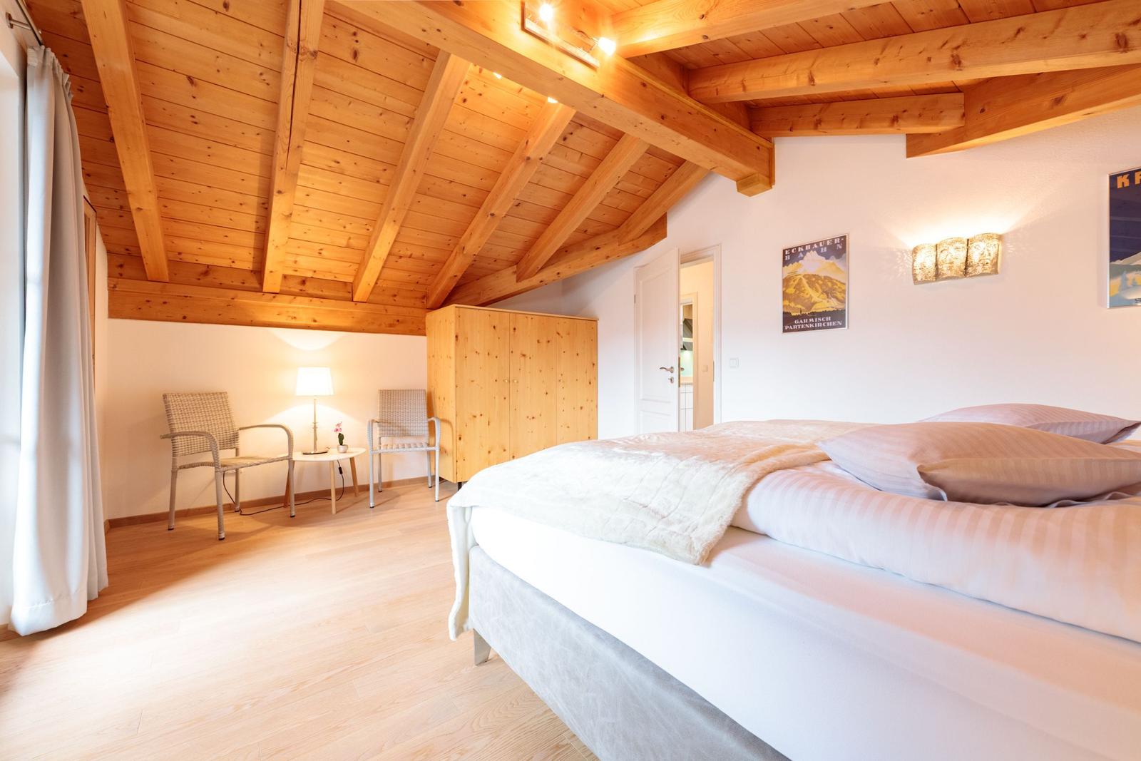 Schlafzimmer mit Holzdecke, Bett, Schrank und zwei Stühlen.