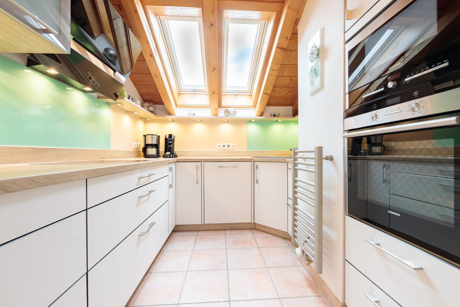 Küche mit weißen Schränken, grüner Rückwand und Dachfenstern.
