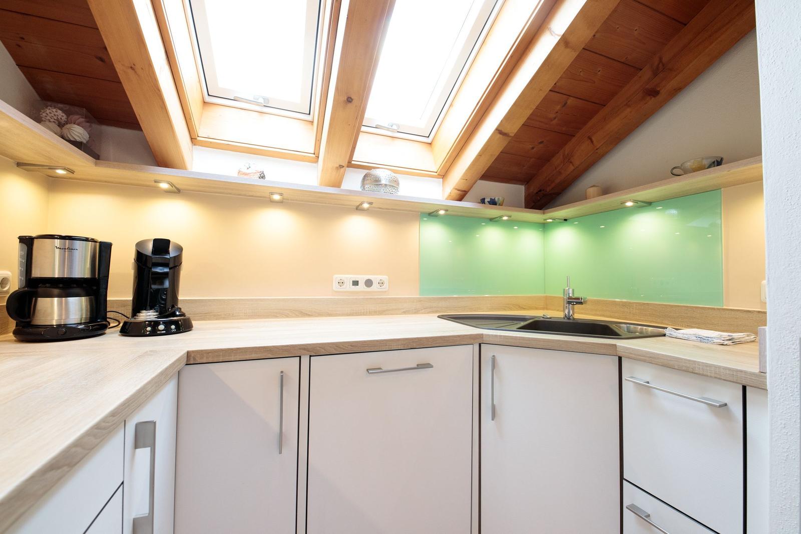 Küche mit Holzdecke, Dachfenstern und grüner Rückwand.