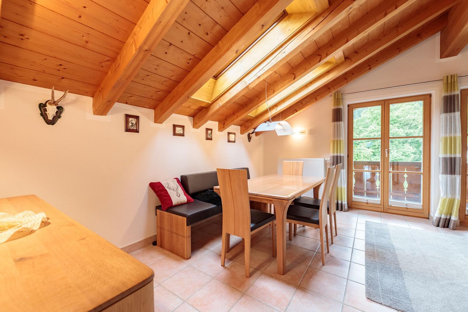 Essbereich mit Holztisch, Stühlen und Sitzbank unter Holzdecke mit Balkonanschluss.