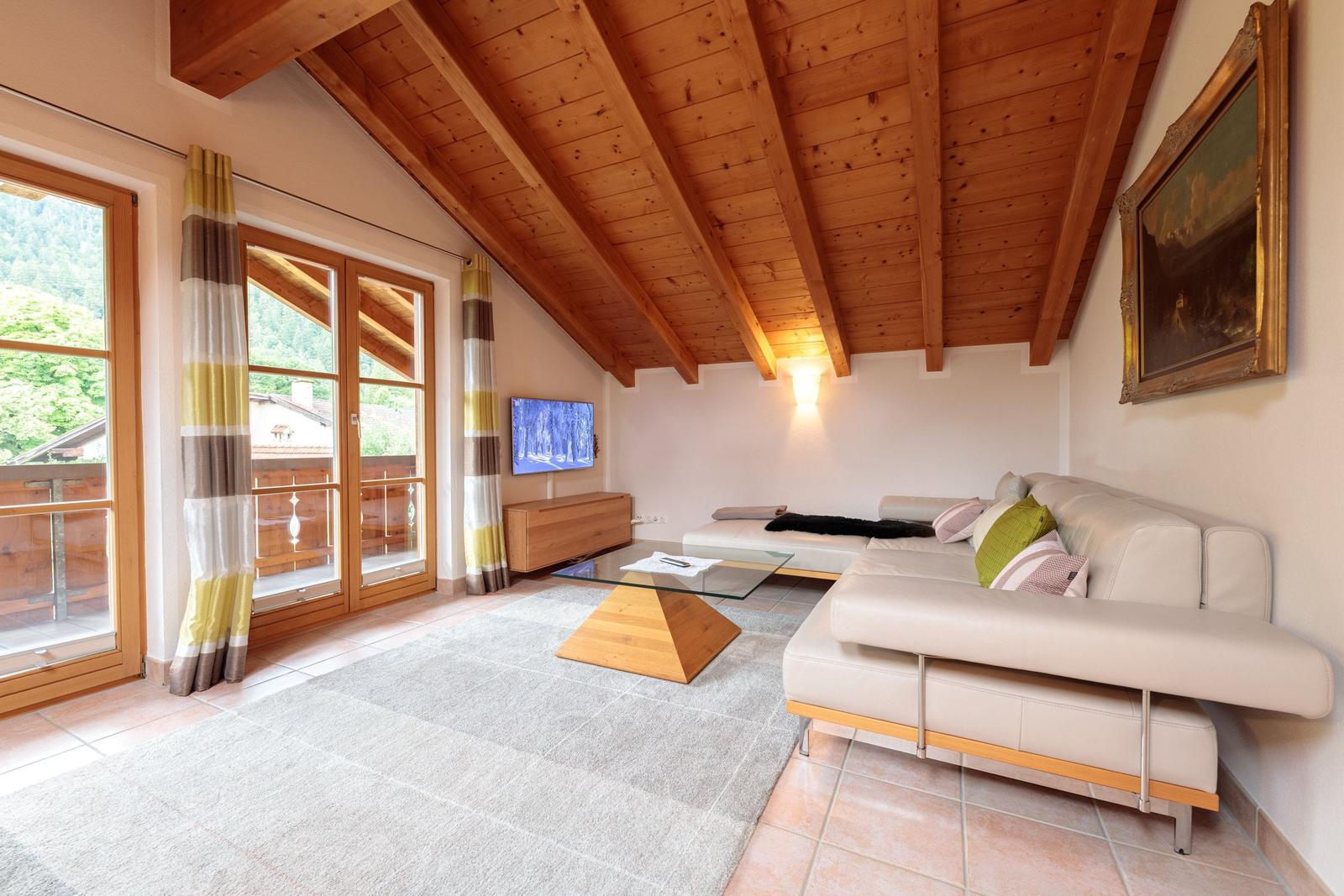 Wohnzimmer mit Holzdecke, Sofa, Couchtisch und Balkonansicht.