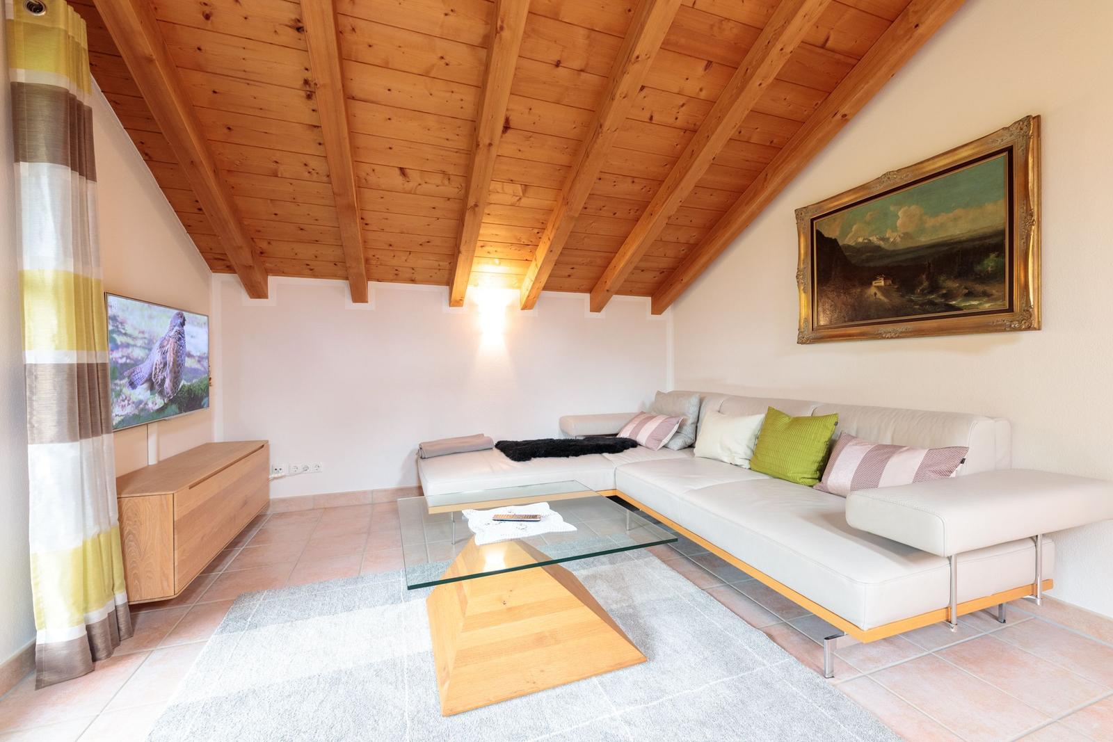 Wohnzimmer mit Sofa, Glas-Tisch und Holzdecke.