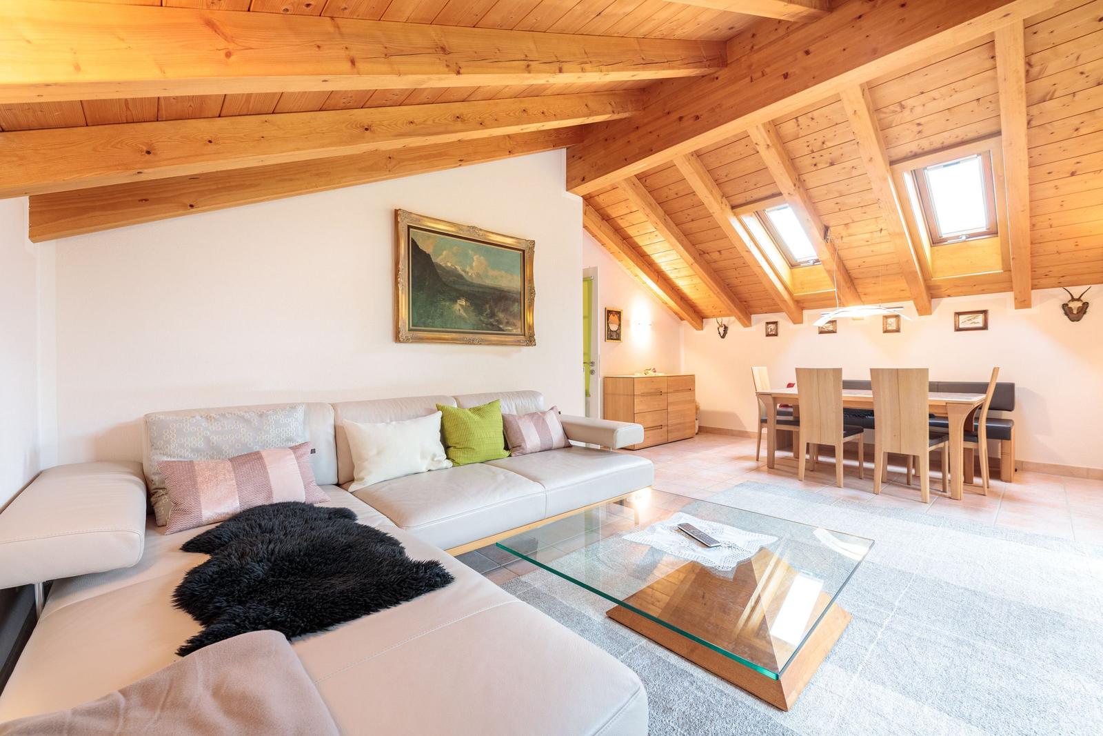 Wohn- und Essbereich mit Holzdecke, Sofa und Glas-Tisch.