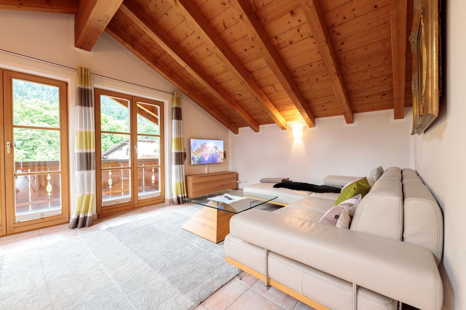 Wohnzimmer mit Holzdecke, Sofa, Glas-Tisch und Balkonansicht.