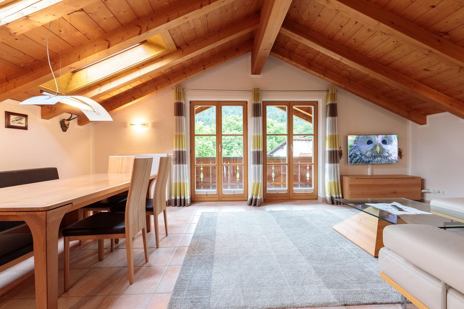 Wohn- und Essbereich mit Holzdecke, TV und Blick auf Balkon.