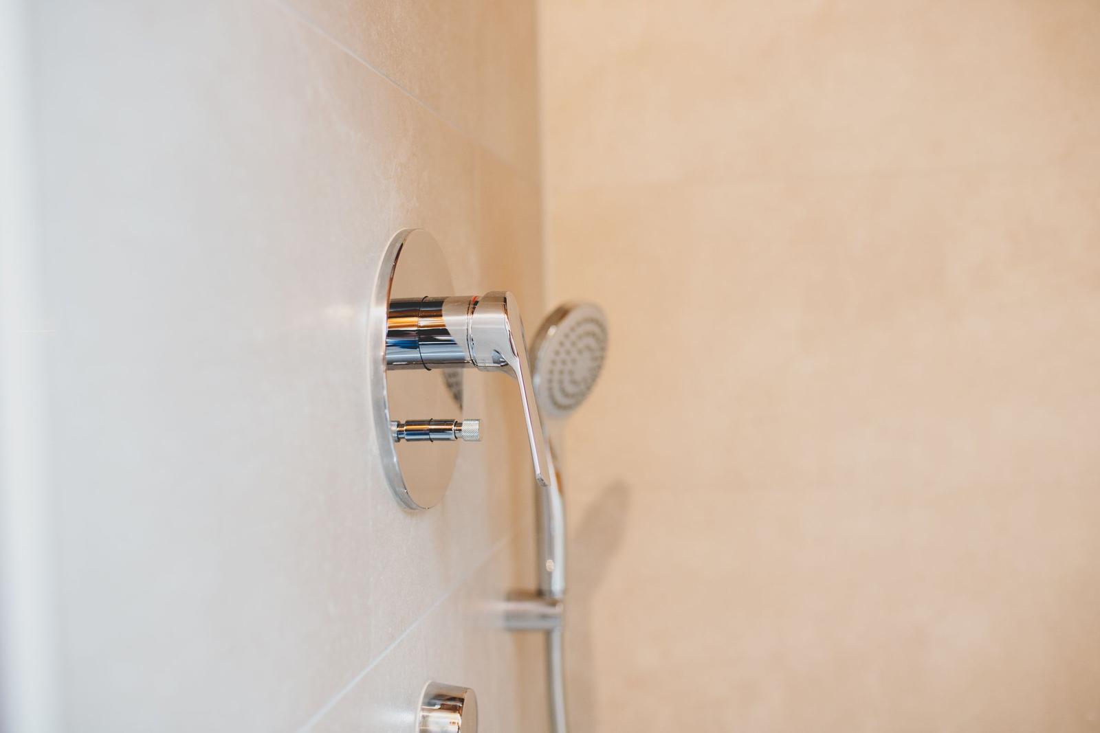 Dusche mit Chromarmatur und Handbrause an hellen Fliesen.