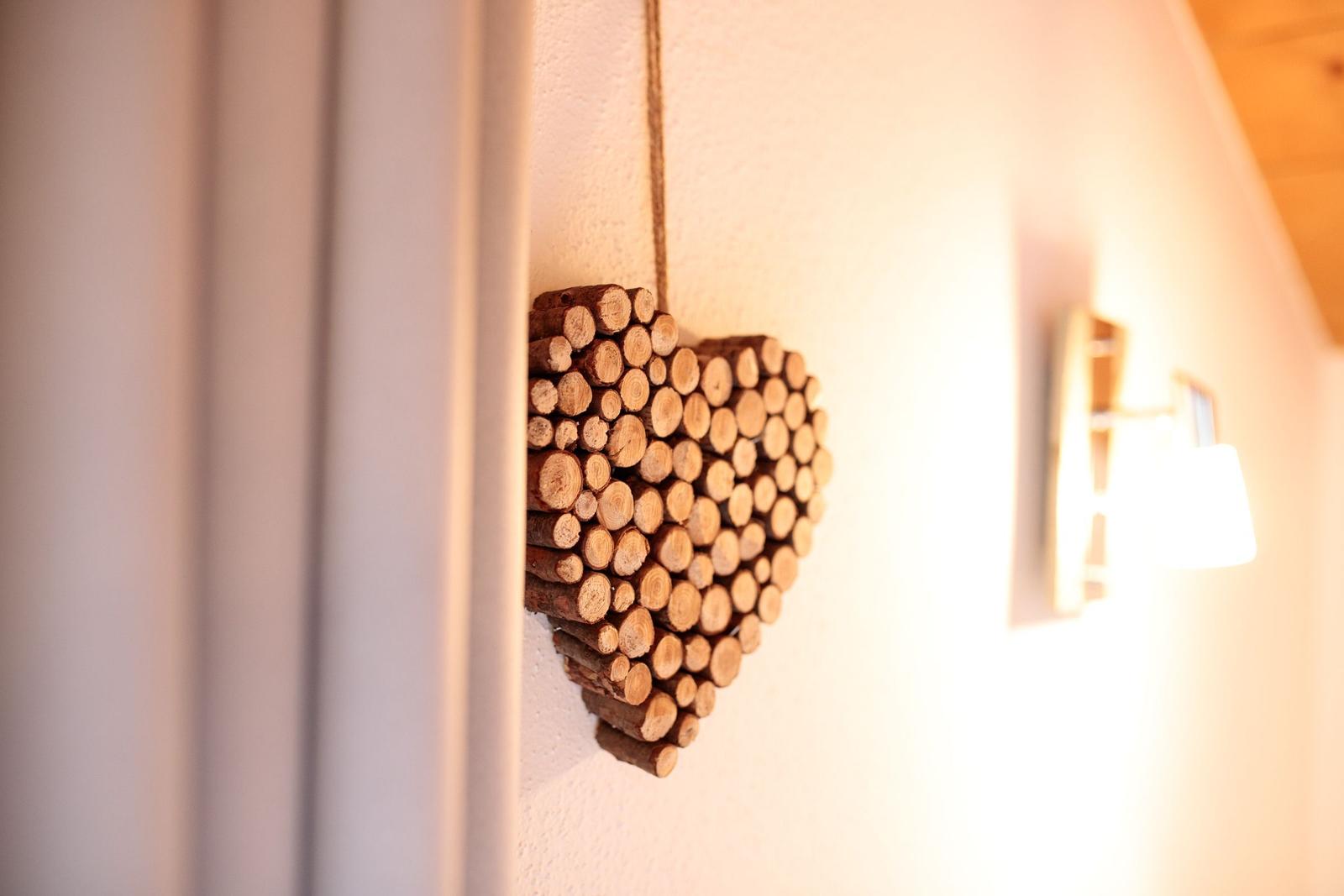 Ein Herz aus Holzstämmchen hängt an der Wand neben einer Lampe.