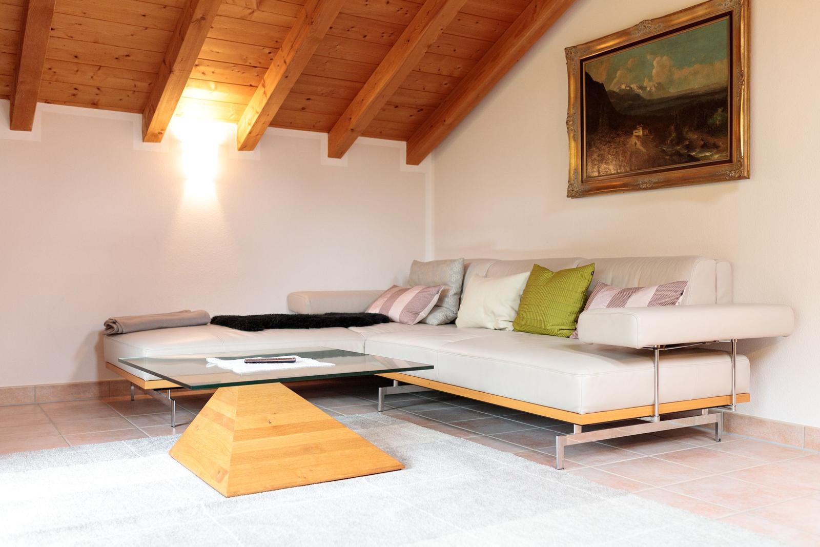 Wohnzimmer mit Sofa, Glas-Tisch und Holzdecke.