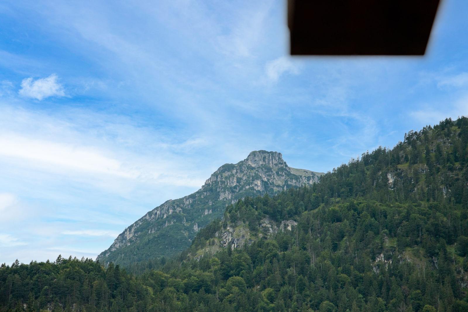Blick auf einen bewaldeten Berg unter blauem Himmel mit weißen Wolken.