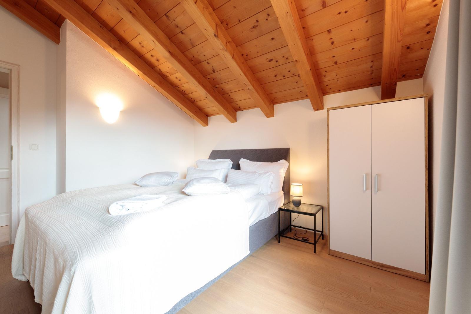 Schlafzimmer mit Holzdecke, Bett, Nachttisch und Kleiderschrank.