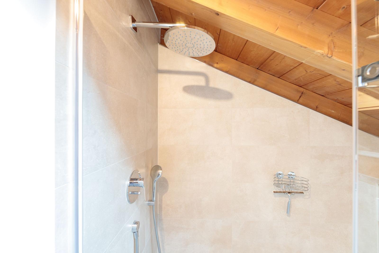 Dusche mit Duschbrause und Handbrause, Holzdecke und Fliesenwand.