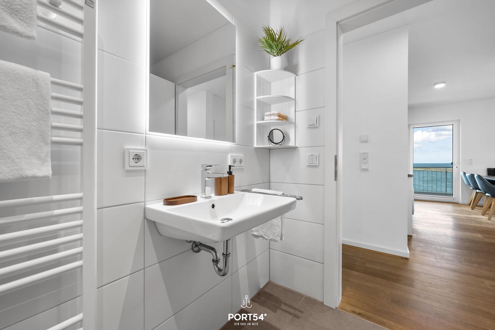 Badezimmer mit Waschbecken, Spiegel und Heizung. Durchgang zur Terrasse mit Meerblick.