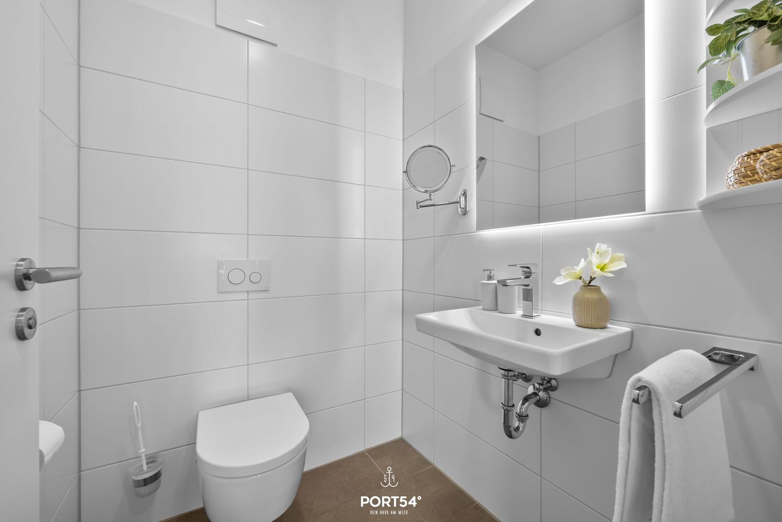 Badezimmer mit Toilette, Waschbecken und Spiegel. Weiße Fliesen und moderne Armaturen.