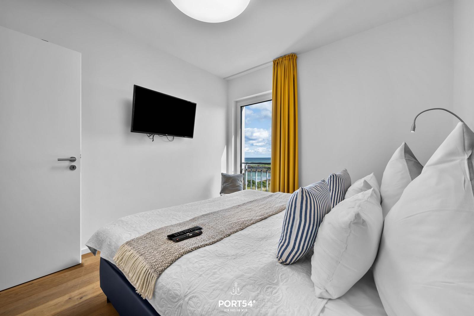 Schlafzimmer mit Blick aufs Meer, TV und gelbe Vorhänge.