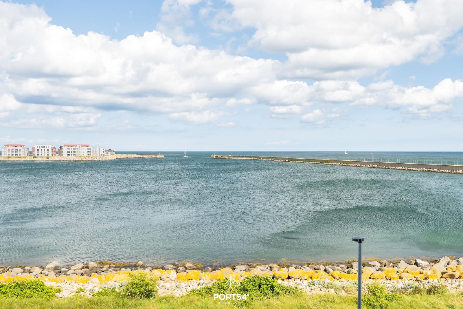 Meeresblick mit Steinhafen und Booten unter blauem Himmel.