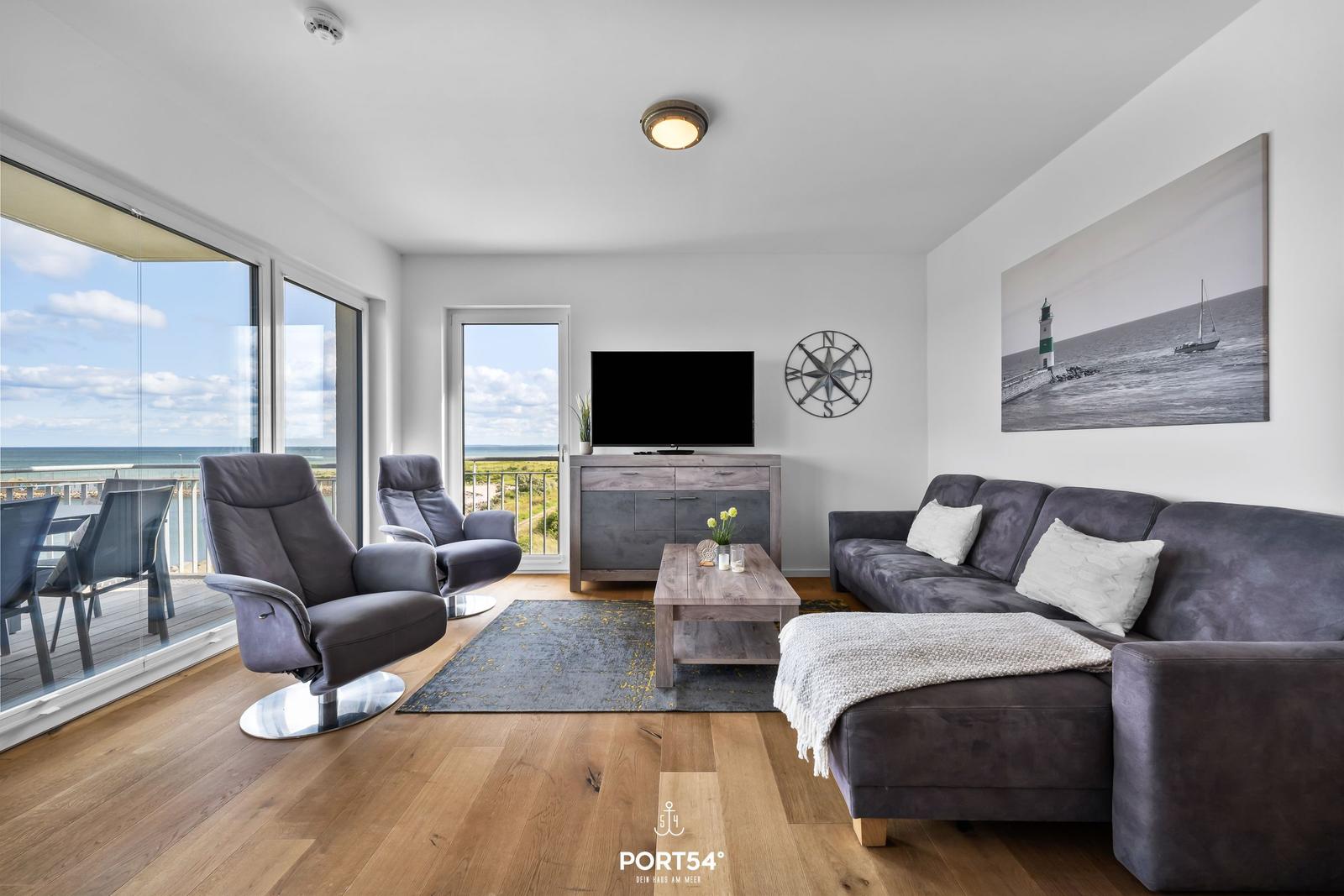 Wohnzimmer mit Sofa, Sesseln und Meerblick über große Fenster.