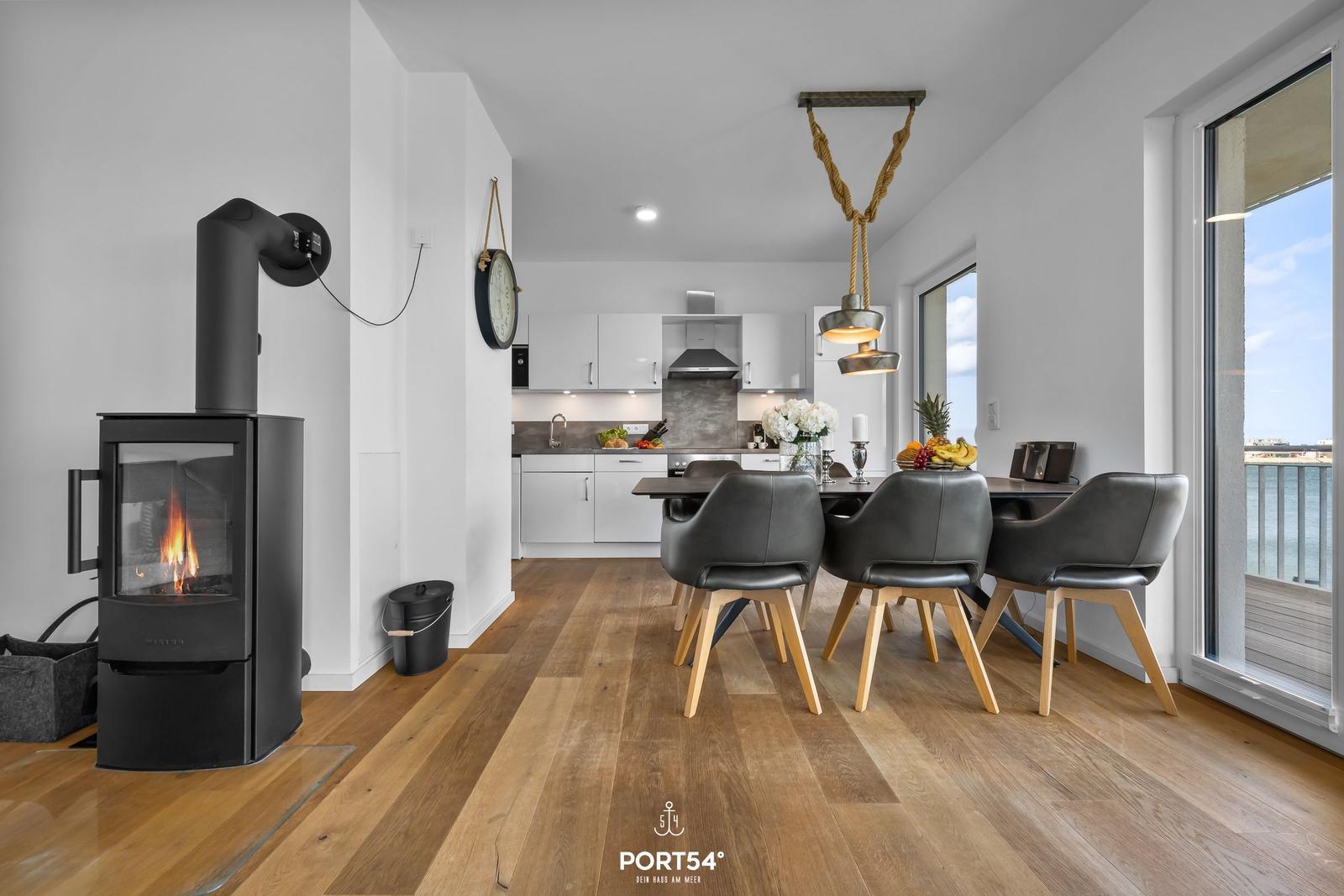 Essbereich mit Blick auf Wasser, schwarze Stühle und Kaminofen im Vordergrund.