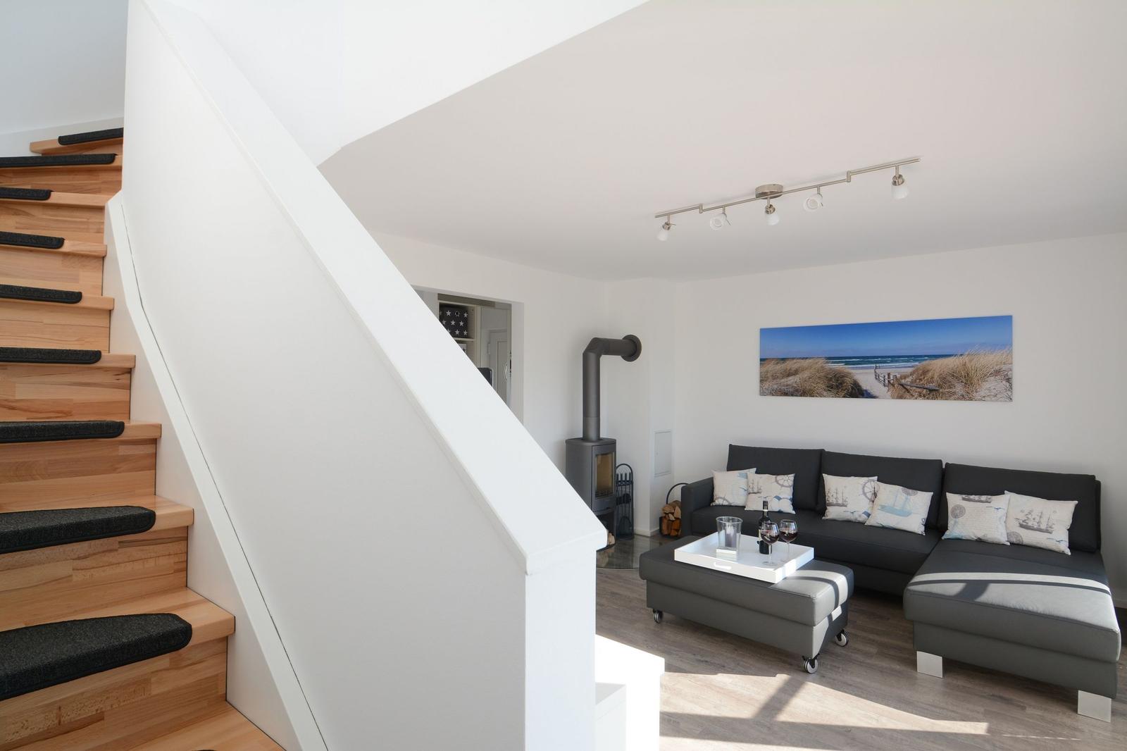 Wohnzimmer mit Sofa, Kamin und Treppe. Wandbild zeigt Strand.