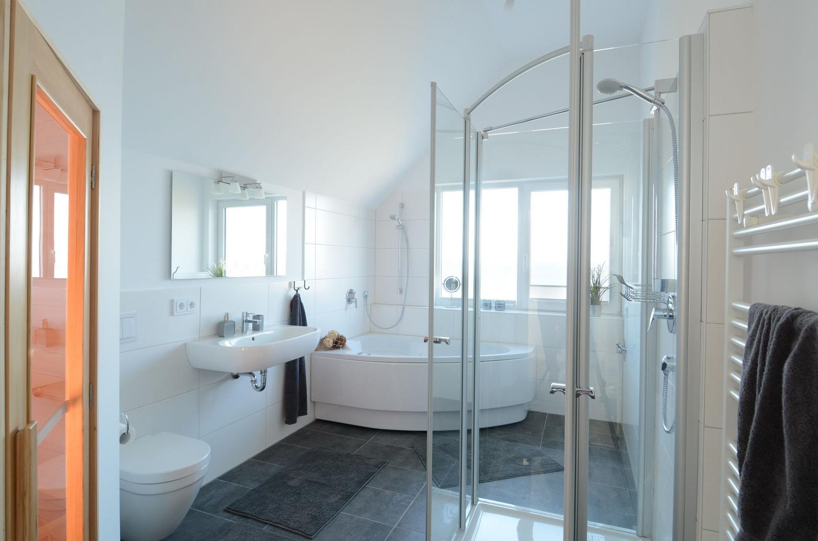 Badezimmer mit Dusche, Badewanne und Toilette. Weiße Wände und dunkle Fliesen.