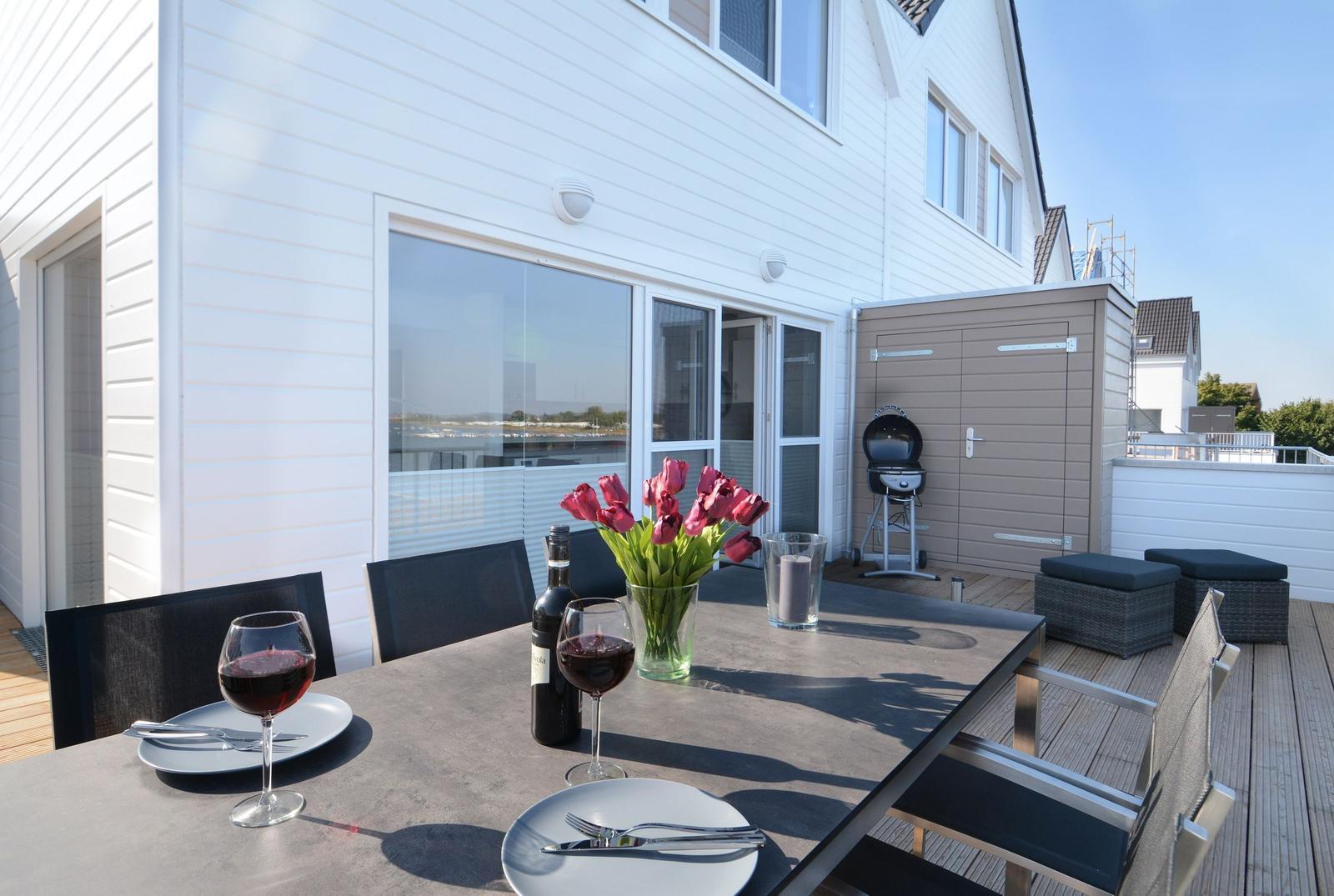 Terrasse mit Tisch, Stühlen, Grill und Blumen.