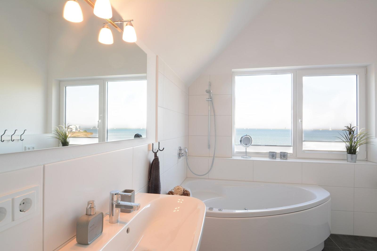 Badezimmer mit Badewanne und Meerblick durch große Fenster.