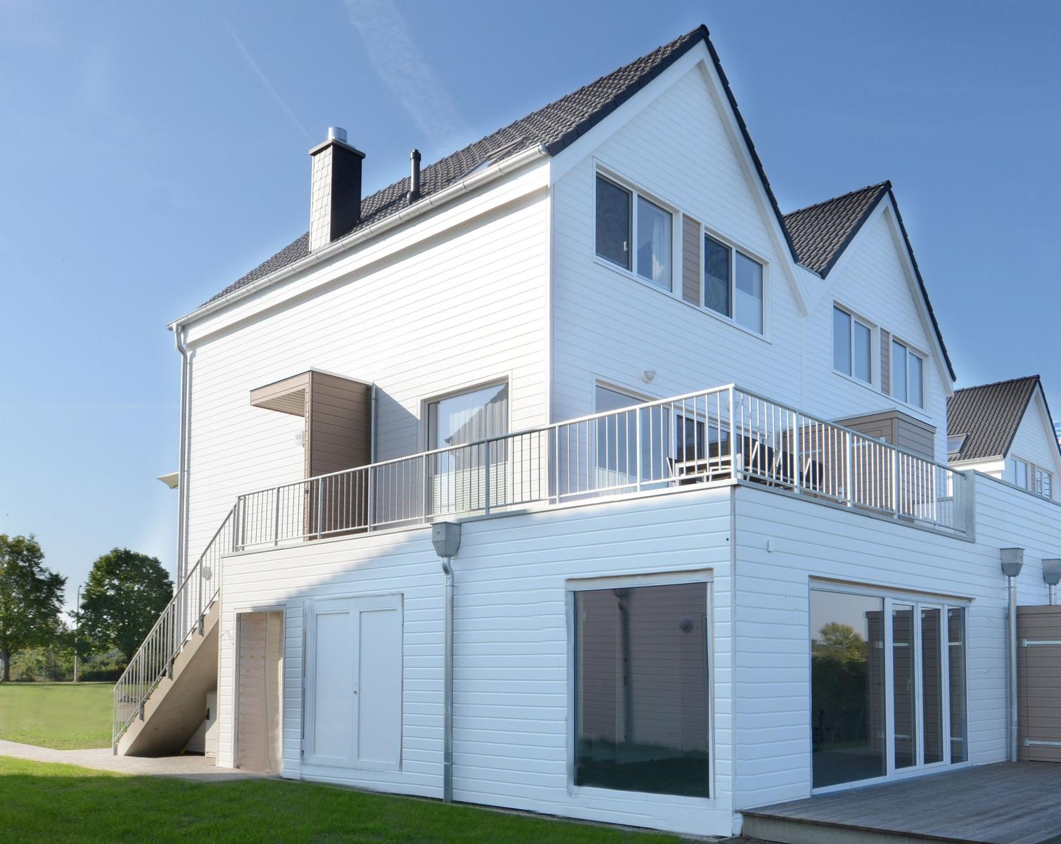 Moderne weiße Villa mit Balkon und Glasfront. Grünfläche und klare Sicht.